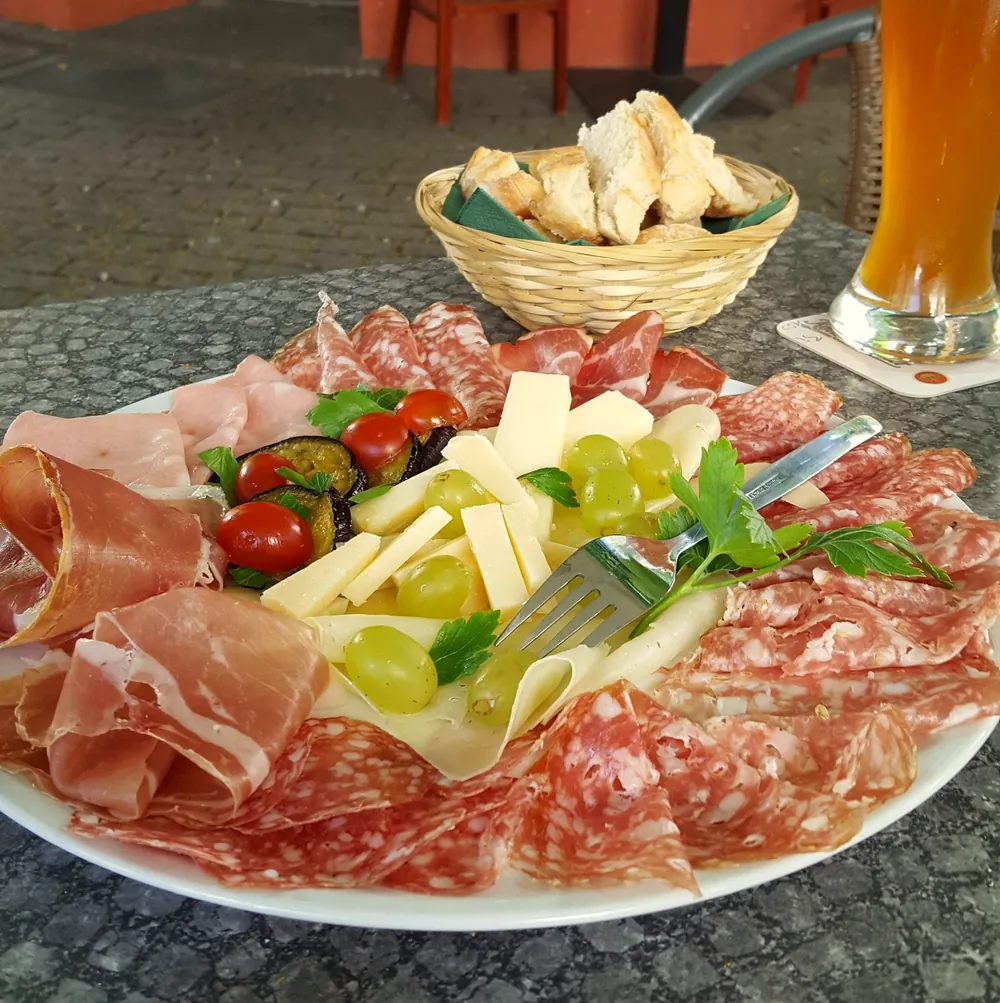 Teller mit Schinken, Salami, Käse, Tomaten und Weintrauben, dazu Brot