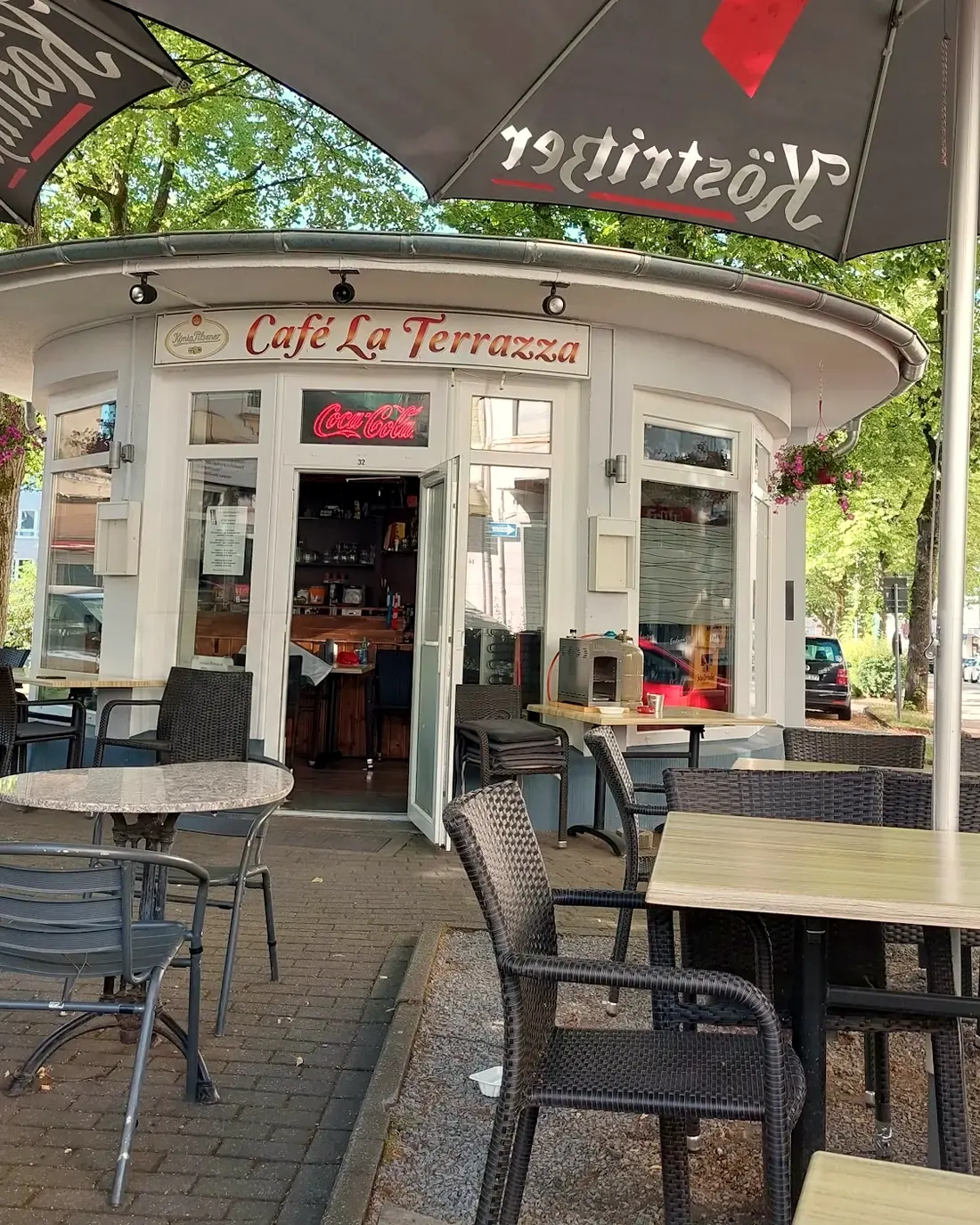 Unser runder weißer Pavillon mit dem Schriftzug, davor Tische und Stühle unter Sonnenschirmen und Bäumen